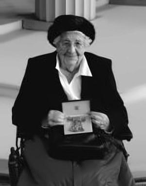 Miss Mary P. Case MBE — a black and white photograph of Mary Case seated, in a dark coat and hat, holding the case containing her MBE