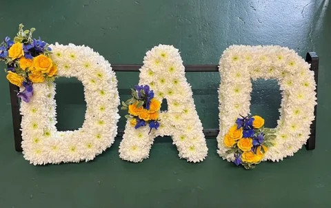 DAD spelt out in white chrysanthemums, dressed with yellow roses and cornflower blue