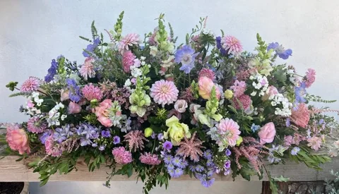 A coffin spray in soft pinks and lilacs — dahlias, roses, snapdragons and scabious, loosely gathered